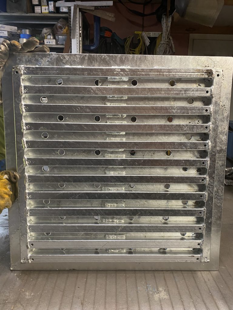 Back view of tube's support grating consisting of 12 bearing tube and 2 banding tubes welded under heavy plate with multiple holes. The plate extends all around past the supporting tube's grating since the drain does not have steel angle support. This large floor drain cover replaced collapsed cover. Galvanized. Please note that each tube has 2 holes for internal wall galvanization inside the tube. JW Investrade Inc. for metalgrating.ca 2023, London, Ontario