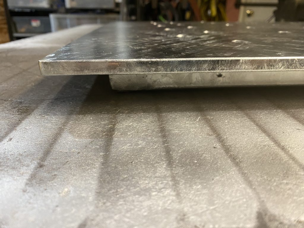 Side view of 12 bearing tube floor drain cover, with 0.38 inch thick steel Q& H plate, galvanized. This heavy plate and and supporting structure below it signifies heavy load capabilities. Please note how much the plate extends beyond tube's supporting structure in order to sustain the load in the drain with no angle steel support. JW Investrade Inc. for metalgrating.ca 2023, London, Ontario