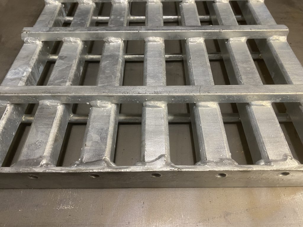 The steel metal grating weldment panel uses boxed sandwich effect to increase its resistance to impact and load aside of increased resistance of hollow square tubes as bearing tubes. The bottom solid square cross rods and top cross round rods perpendicularly welded on opposite sides of each bearing tube sandwich the panel. The banding bar is drilled to allow galvanization process inside each tube. JW Investrade Inc. for metalgrating.ca 2023, London, Ontario.