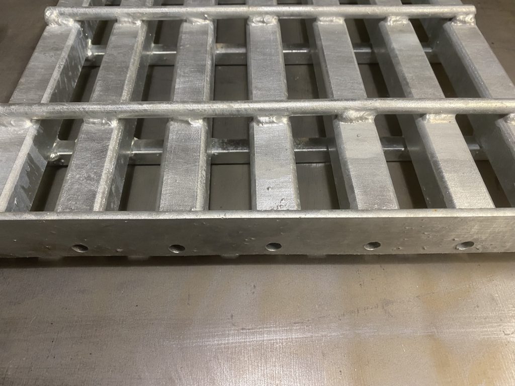 The steel metal grating weldment panel uses boxed sandwich effect to increase its resistance to impact and load aside of increased resistance of hollow square tubes as bearing tubes. The bottom solid square cross rods and top round rods perpendicularly welded on opposite sides sandwich the bearing tubes. The banding bar is drilled to allow galvanization process inside each tube. JW Investrade Inc. for metalgrating.ca 2023, London, Ontario.