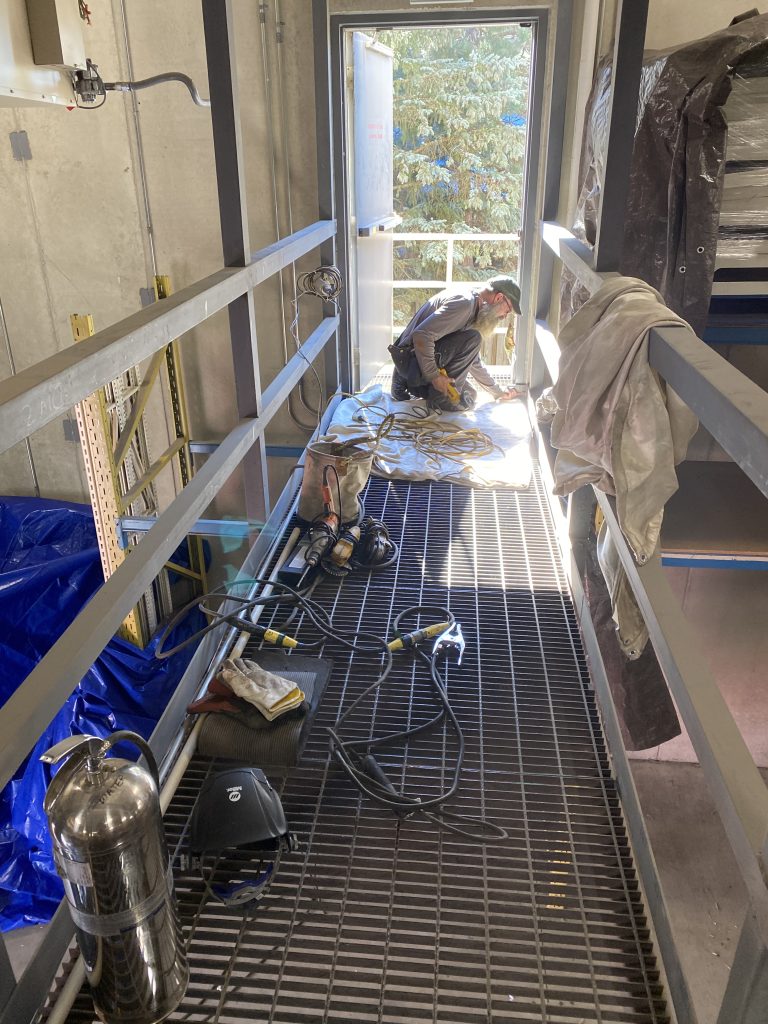 The grate steel on catwalk must be stabilized to provide stable support for workers going to emergency exit. Catwalks must also be stabilized to avoid horizontal movements. The image shows the worker stabilizing grate steel to catwalk structure and stabilizing the whole catwalk.JW Investrade Inc. for metalgrating.ca 2020, London, Ontario.